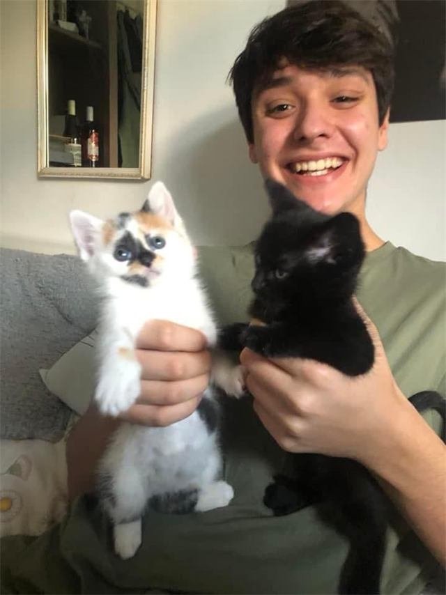 A smiling young man holding up a calico kitten and a black kitten