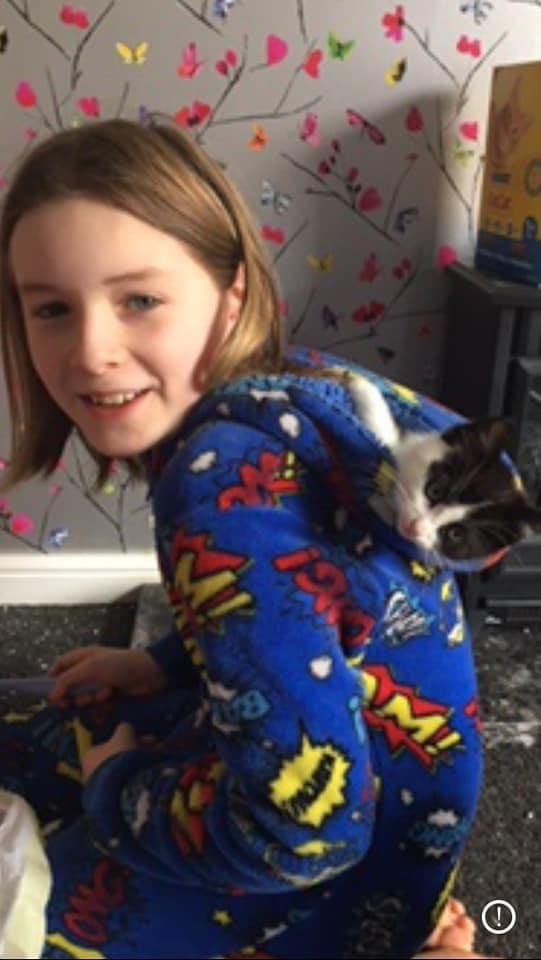 A smiling girl with a black and white kitten peeping out of her hood