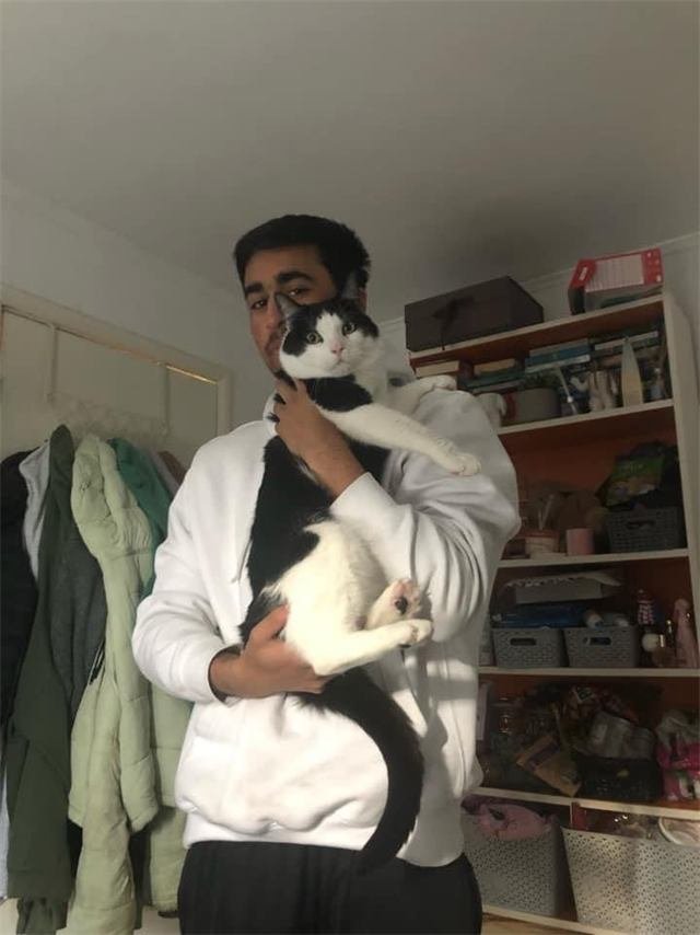 A young man holding a black and white cat up against his shoulder
