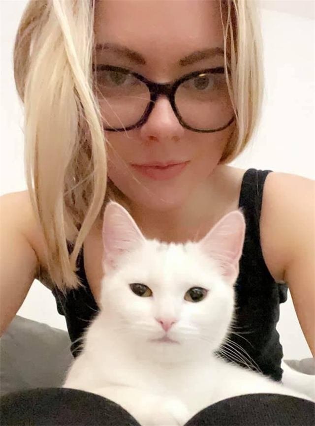 A white cat sitting in front of a woman in glasses