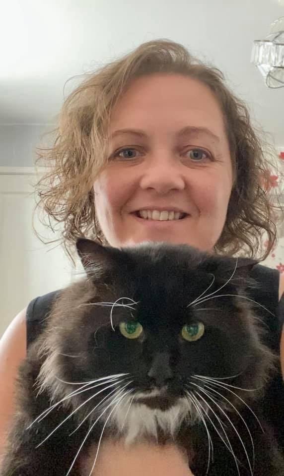 A smiling foster carer holding a fluffy black and white cat