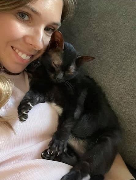 A black kitten asleep on a smiling woman's chest