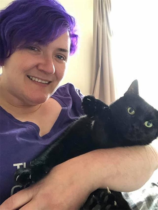 A woman with purple hair cuddling a black cat with green eyes