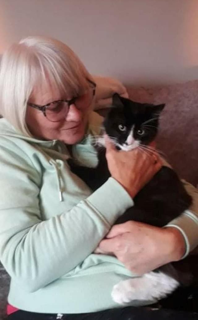 A woman with white hair cuddling a black and white cat