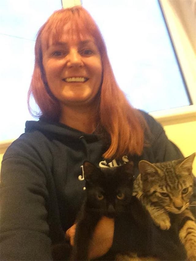 A smiling woman holding a black kitten and a tabby kitten