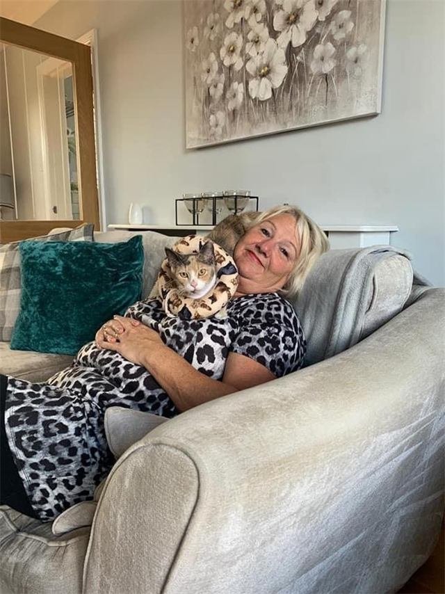 A tortoiseshell cat in a soft recovery collar resting on a woman's shoulder