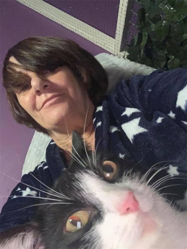 A black and white cat with amber eyes lying on a woman in a star-print dressing gown