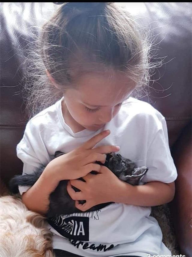 A young girl gently cradling a tiny black kitten